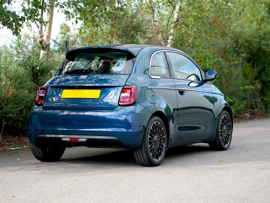 Rear three-quarter view of an ocean green FIAT 500e parked on a country road