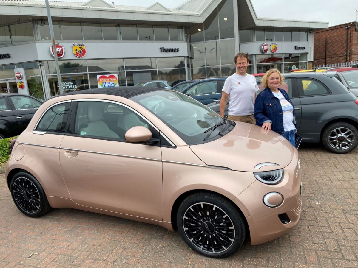 Owners smiling next to a rose gold FIAT 500e at a Thames dealership handover collection
