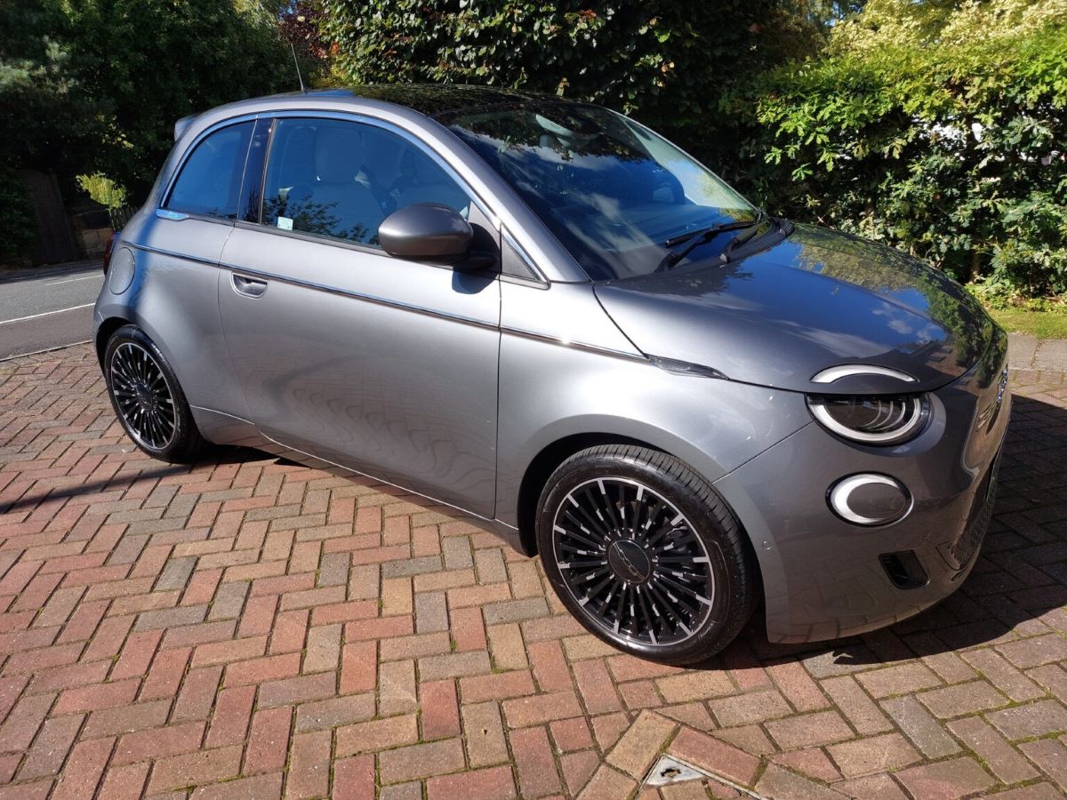 Front three-quarter view of a grey FIAT 500e La Prime parked on a brick driveway