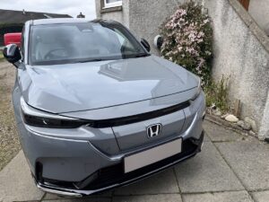 Front view of a 2025 Honda e:NY1 Advance electric SUV finished in Urban Grey Pearl parked on a driveway