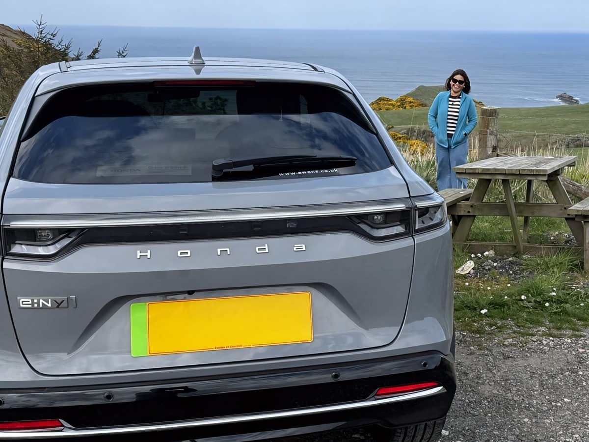 Rear view of a 2025 Honda e:NY1 Advance parked by a coastal picnic bench overlooking the sea