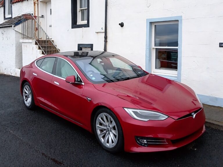 A 2017 Tesla Model S 75kWh finished in Red Multi-Coat with panoramic glass roof parked outside traditional cottages in Scotland
