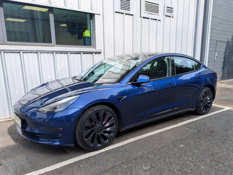 Side profile of a blue 2021 Tesla Model 3 parked in a designated bay.