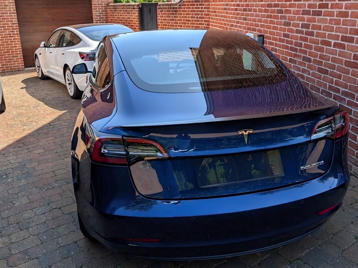 Rear view of a blue 2021 Tesla Model 3 parked on a brick driveway.